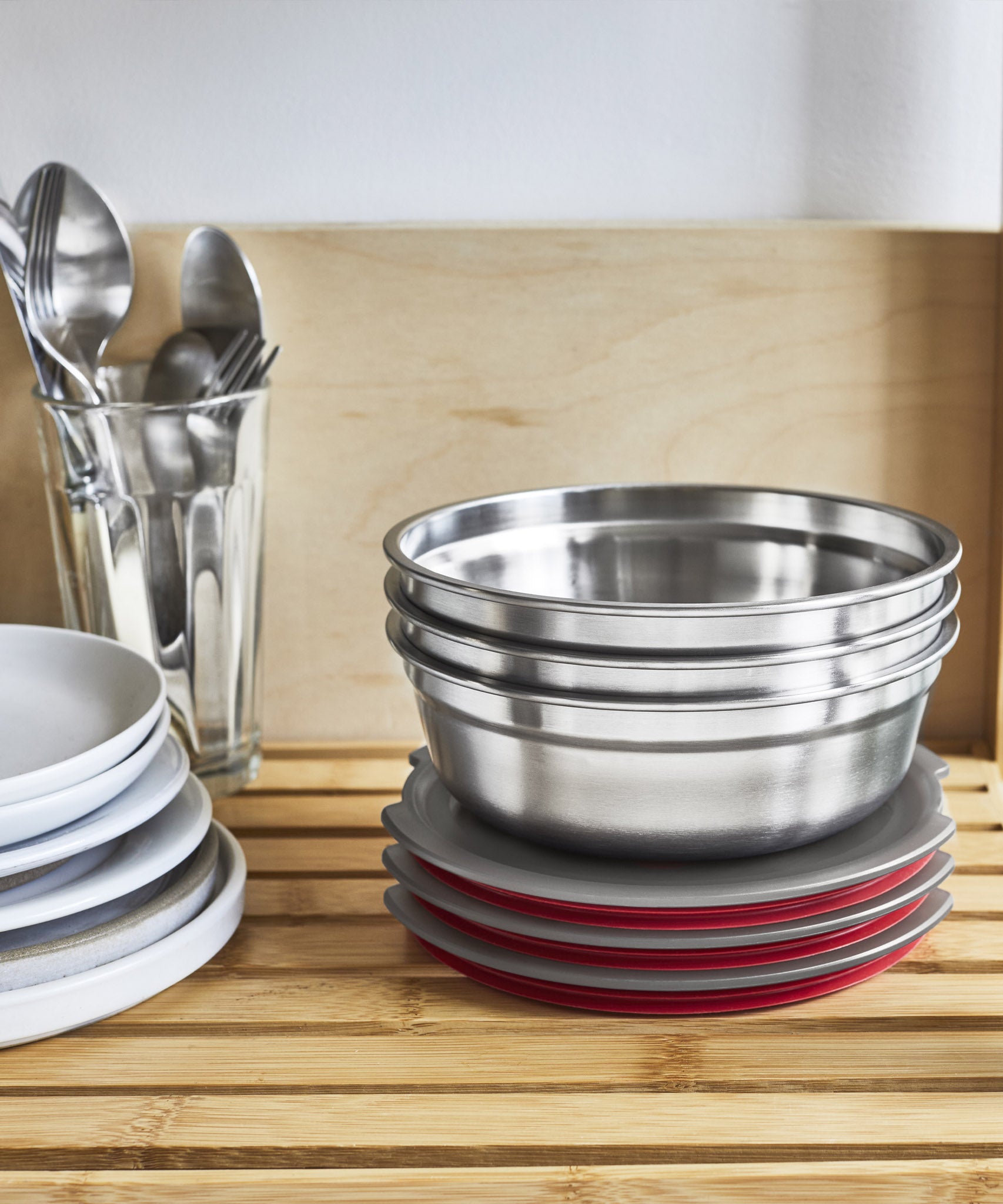 A close up of 3 Black + Blum stainless steel bowls on a wooden racking with the lids resting underneath