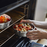 A close up of an adult holding a small Black + Blum stainless steel bowl with food inside and putting it in a oven