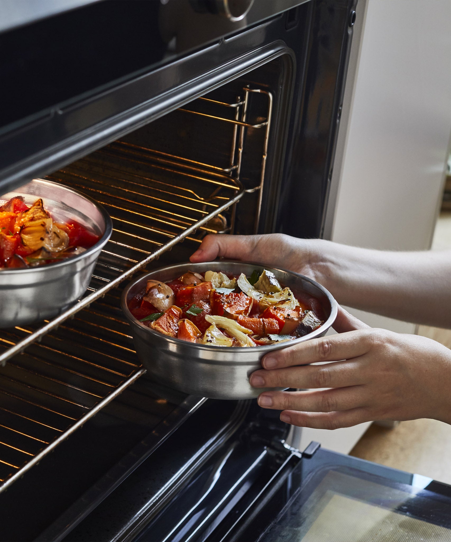 A close up of an adult holding a small Black + Blum stainless steel bowl with food inside and putting it in a oven