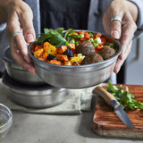 A close up of an adult holding a small Black + Blum stainless steel bowl with food inside