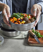 A close up of an adult holding a small Black + Blum stainless steel bowl with food inside