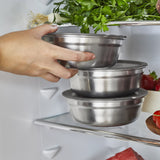 A close up of an adult holding a small Black + Blum stainless steel bowl and putting it in a fridge.