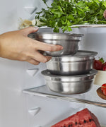 A close up of an adult holding a small Black + Blum stainless steel bowl and putting it in a fridge.