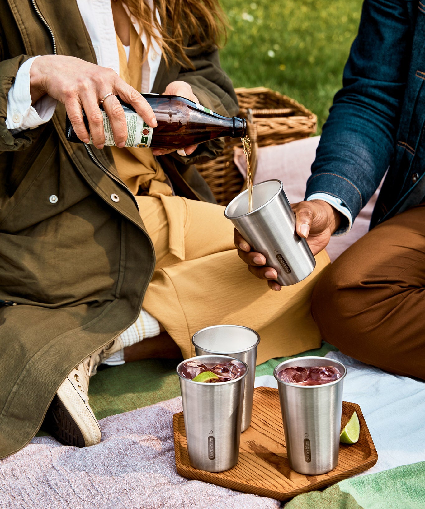A close up of a couple of adults having a picnic and pouring drink into the Black + Blum stainless steel cups