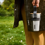 A close up of an adult holding the Black + Blum stainless cup set by the handy black strap handle