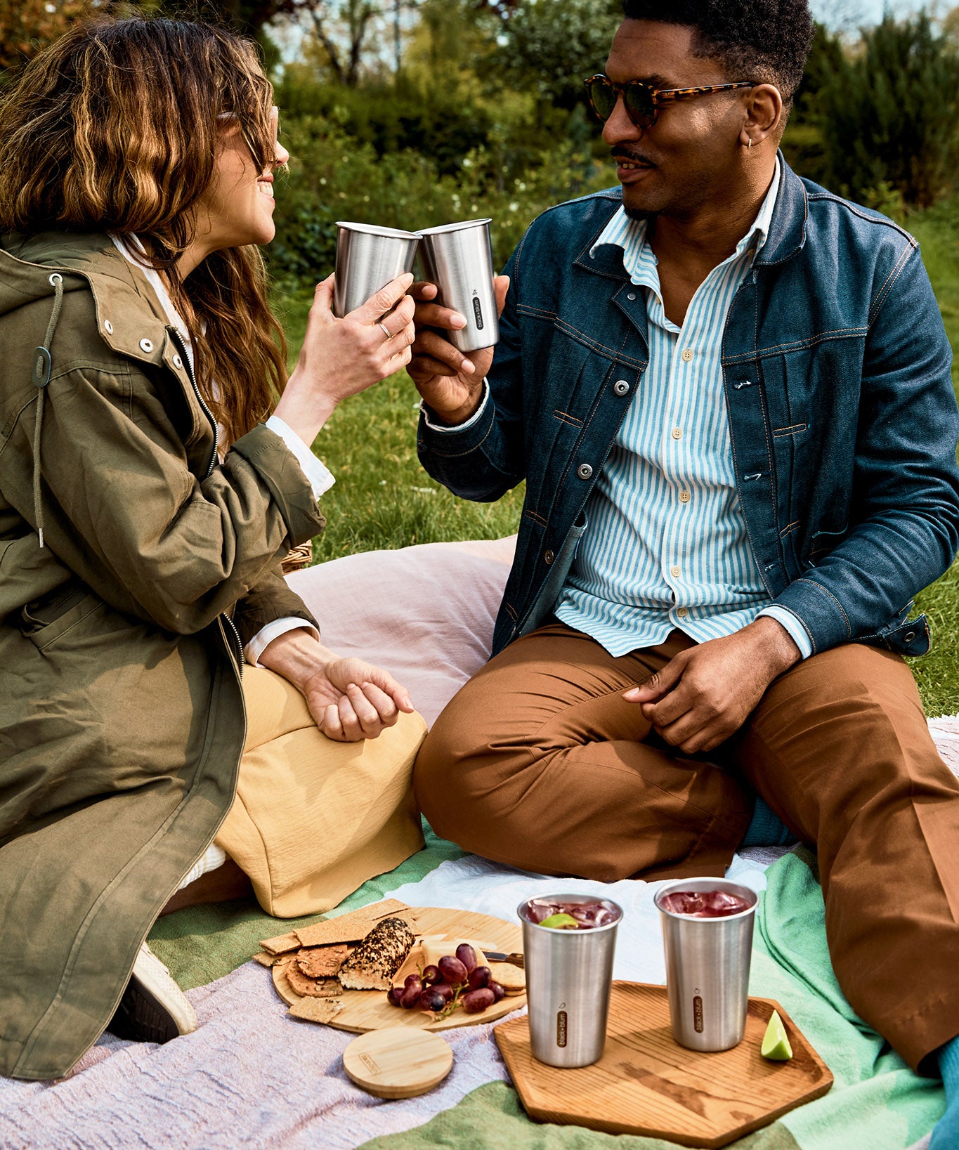 A couple of adults having a picnic outside and holding the Black + Blum stainless steel cups