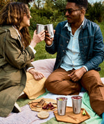 A couple of adults having a picnic outside and holding the Black + Blum stainless steel cups