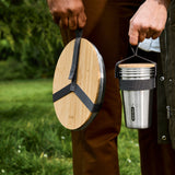 A close up of an adult holding the Black + Blum stainless steel plate and cup set by the handy black strap handle