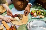 A close up of a couple of  adult having a picnic and using the Black + Blum stainless steel plates and using the bamboo lid as a chopping board