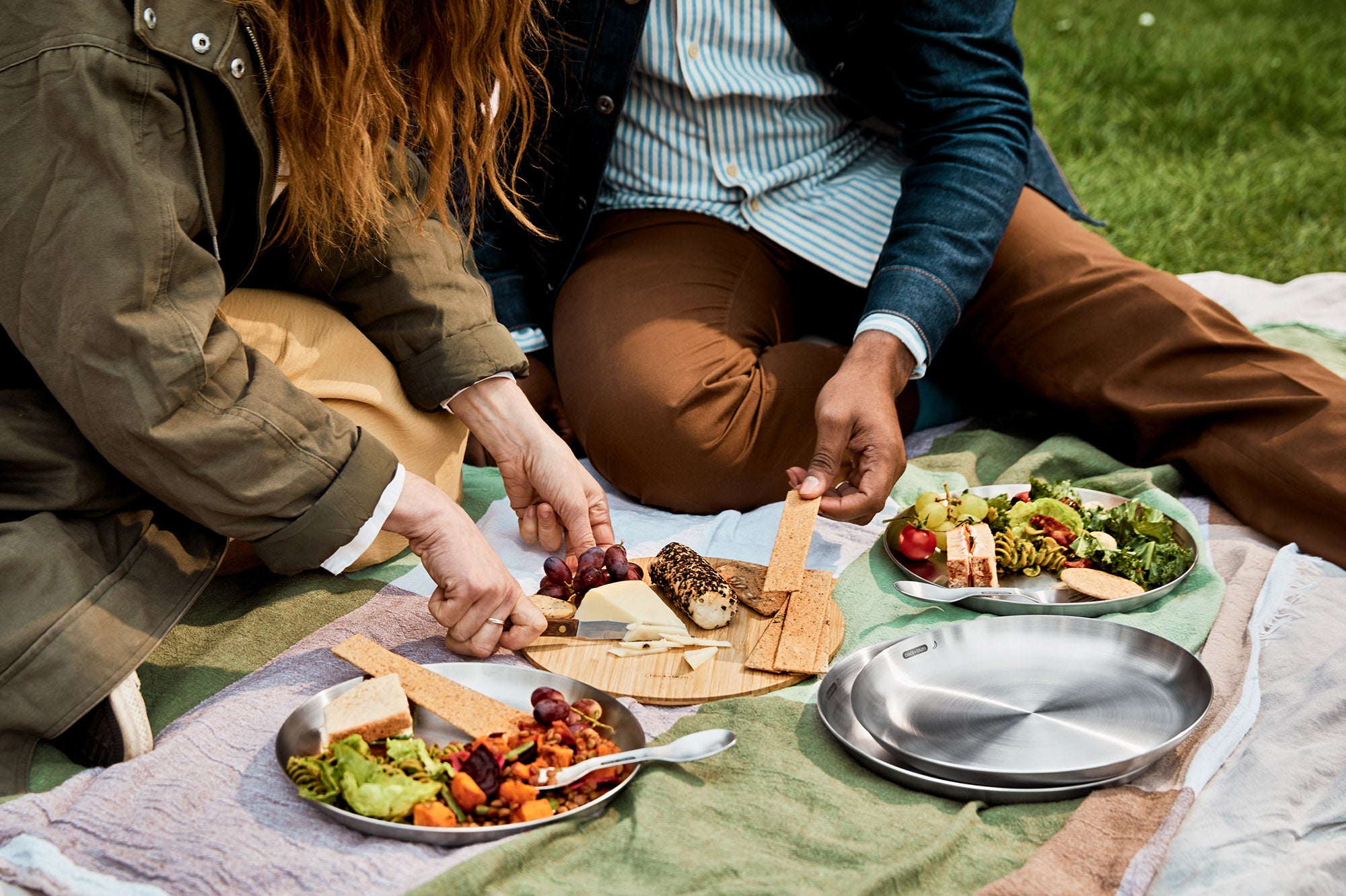 A close up of a couple of  adult having a picnic and using the Black + Blum stainless steel plates and the bamboo lid to serve food