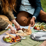 A close up of a couple of  adult having a picnic and using the Black + Blum stainless steel plates and the bamboo lid to serve food