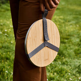 A close up of an adult holding the Black + Blum stainless steel plate by the handy black strap handle and showing the protective bamboo lid detail