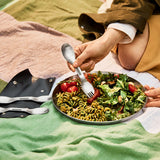 A close up of an adult holding a spork and eating off the Black + Blum stainless steel plate