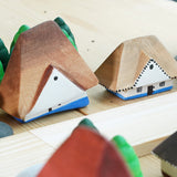 Close up of the Bumbu solid wooden Bucovina house toys on a wooden table next to some grapat mandala trees