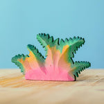 Bumbu Wooden Fern Bush pictured in an adult's hand in front of a blue wall