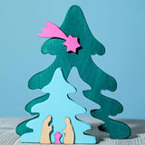 A Bumbu Christmas Tree Nativity Puzzle in a Fuchsia colour way placed on a wooden surface. The blue tree piece has been pulled to the front.