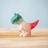 A Bumbu Toys Baby Carnotaurus wooden toy dinosaur figure placed on a wooden surface.