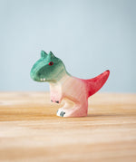 A Bumbu Toys Baby Carnotaurus wooden toy dinosaur figure placed on a wooden surface.