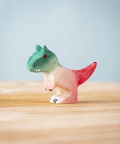 A Bumbu Toys Baby Carnotaurus wooden toy dinosaur figure placed on a wooden surface.