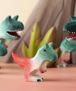 A Bumbu Toys Baby Carnotaurus dinosaur placed at the front of a small world play scene with other handmade wooden toys from Bumbu in the background.