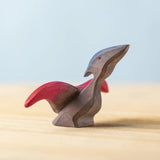 A Bumbu Toys handmade Baby Pterandon wooden figure placed on a wooden surface. This Baby Pterandon figure is part of a varied collection of wooden figures available at Babipur.