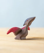 A Bumbu Toys handmade Baby Pterandon wooden figure placed on a wooden surface. This Baby Pterandon figure is part of a varied collection of wooden figures available at Babipur.