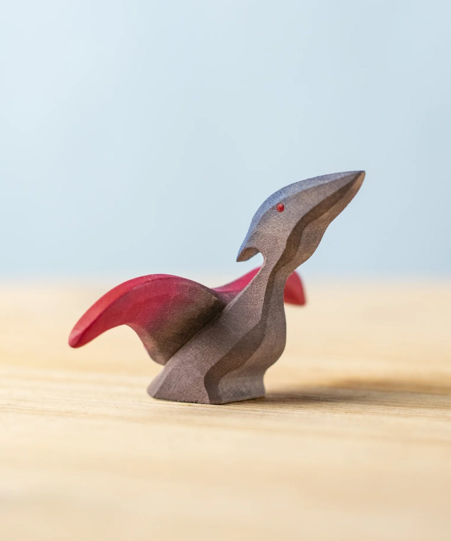 A Bumbu Toys handmade Baby Pterandon wooden figure placed on a wooden surface. This Baby Pterandon figure is part of a varied collection of wooden figures available at Babipur.