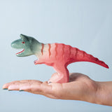 A Bumbu Toys Big Carnotaurus dinosaur figure shown in an adult's hand. The handmade figures and many other wooden animals are available here at Babipur.