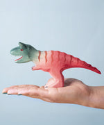 A Bumbu Toys Big Carnotaurus dinosaur figure shown in an adult's hand. The handmade figures and many other wooden animals are available here at Babipur.