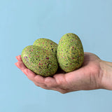 A close up of an adult holding the three bumbu t-rex eggs in their hand against a blue background.