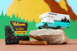 Candylab wooden campervan toy on top of a grey rock in front of a colourful mountain background