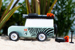 Side of the candylab wooden zebra drifter vehicle toy on some sand in front of a green plant