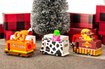 6 wooden Candylab toy trucks lined up on a brown carpet in front of a Christmas tree and some red presents