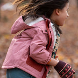 Child in a pink little green radicals coat and gloves walking through a forest with autumn leaves