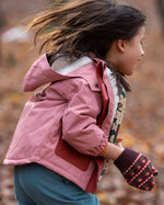 Child in a pink little green radicals coat and gloves walking through a forest with autumn leaves