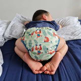 A baby wearing The Close Pop-In +bamboo reusable cloth nappy with adjustable velcro closures, in an orangutan print
