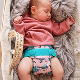 A baby wearing the Close Pop-In +bamboo reusable cloth nappy with adjustable velcro closures, in a ferret print