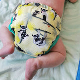 A baby wearing The Close Pop-In +bamboo reusable cloth nappy with adjustable velcro closures, in a lemur print
