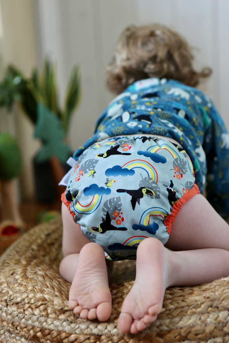 A baby wearing The Close Pop-In +bamboo reusable cloth nappy with adjustable popper closures, in a toucan print