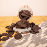 Overturned glass jar of Cocoa Loco vegan dark chocolate buttons on a wooden table