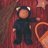 Olli Ella Carson Cat Dinky Dinkum Doll. This soft toy is a black cat with glow in the dark inner ears and a small embroidered rainbow detail on the chest. The cat has been placed in the middle of a Halloween themed flatlay. These soft toys are part of Olli Ella's Halloween collection available here at Babipur.