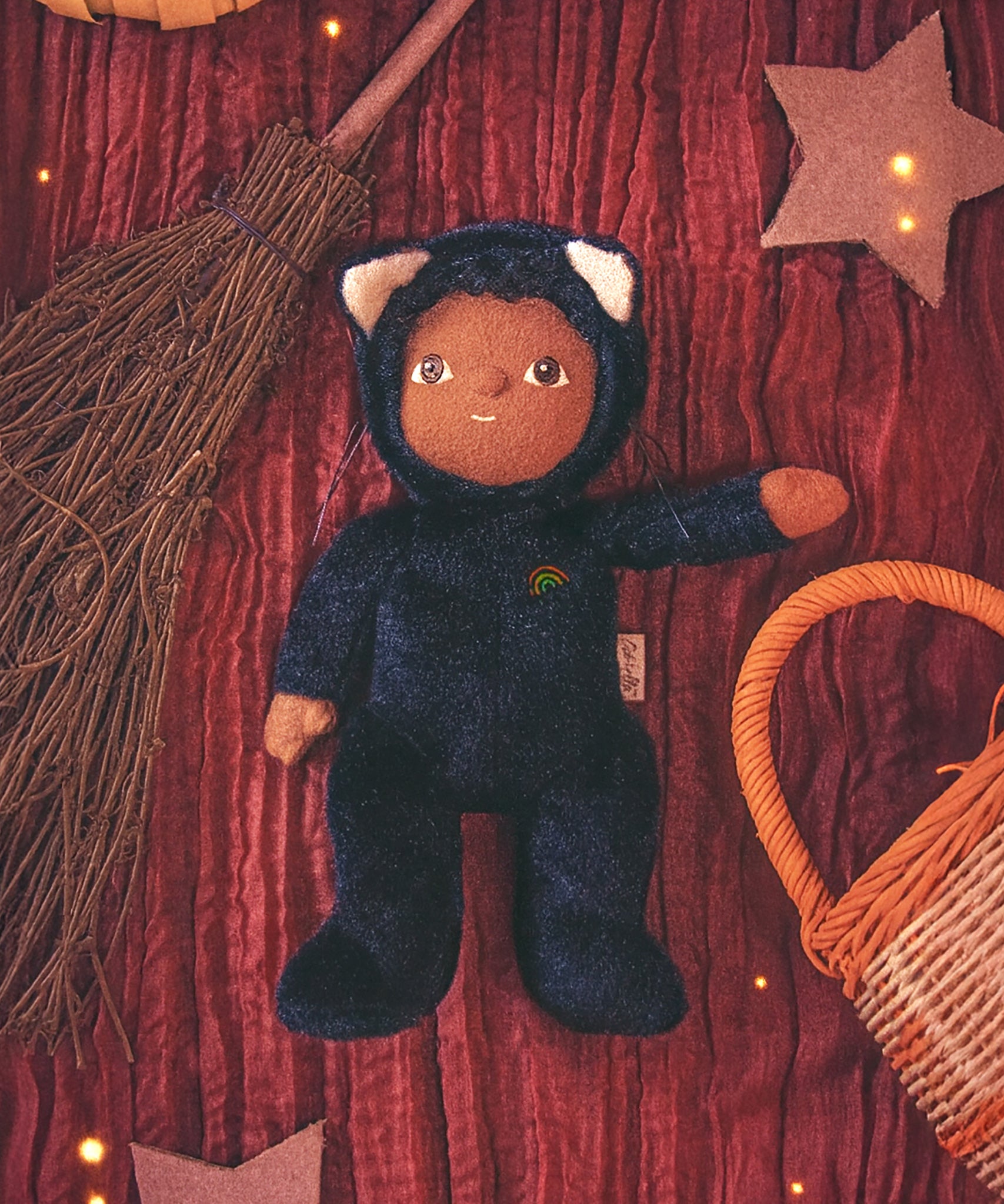 Olli Ella Carson Cat Dinky Dinkum Doll. This soft toy is a black cat with glow in the dark inner ears and a small embroidered rainbow detail on the chest. The cat has been placed in the middle of a Halloween themed flatlay. These soft toys are part of Olli Ella's Halloween collection available here at Babipur.