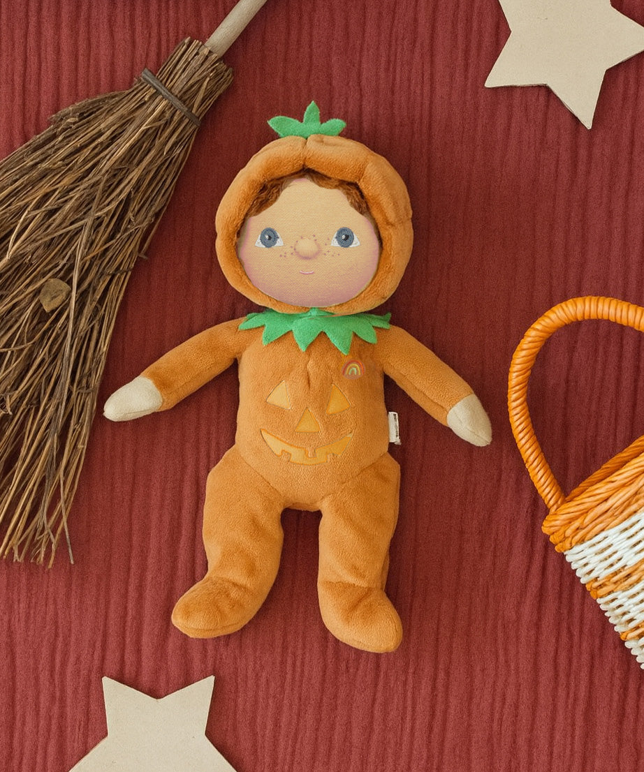 A flatlay image including the Olli Ella Jack-O-Lantern pumpkin dinky dinkum doll. next to a broomstick and basket. Doll is available at Babipur.