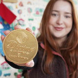Close up of woman holding up the Divine giant Fairtrade milk chocolate coin in front of a white patterned wall