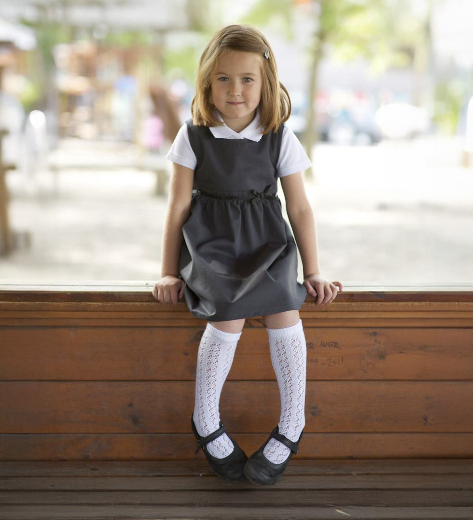 A little girl wearing the Eco Outfitters organic and fair trade cotton school pinafore dress in grey with a bow detail.