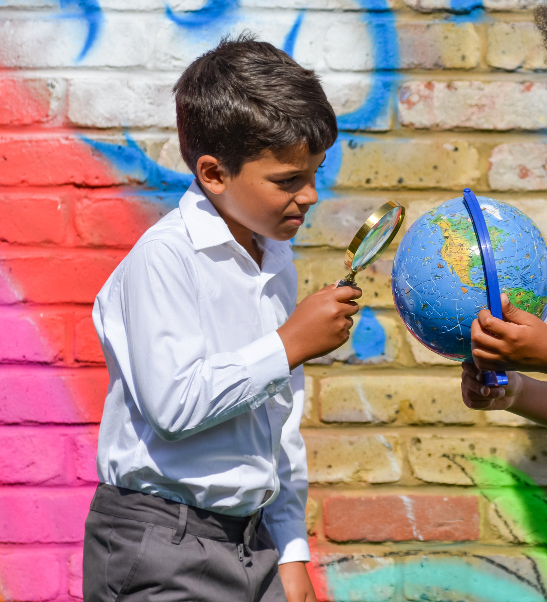 A boy wearing The Eco Outfitters Fair Trade and organic cotton school uniform shirt, and holding a magnifying glass