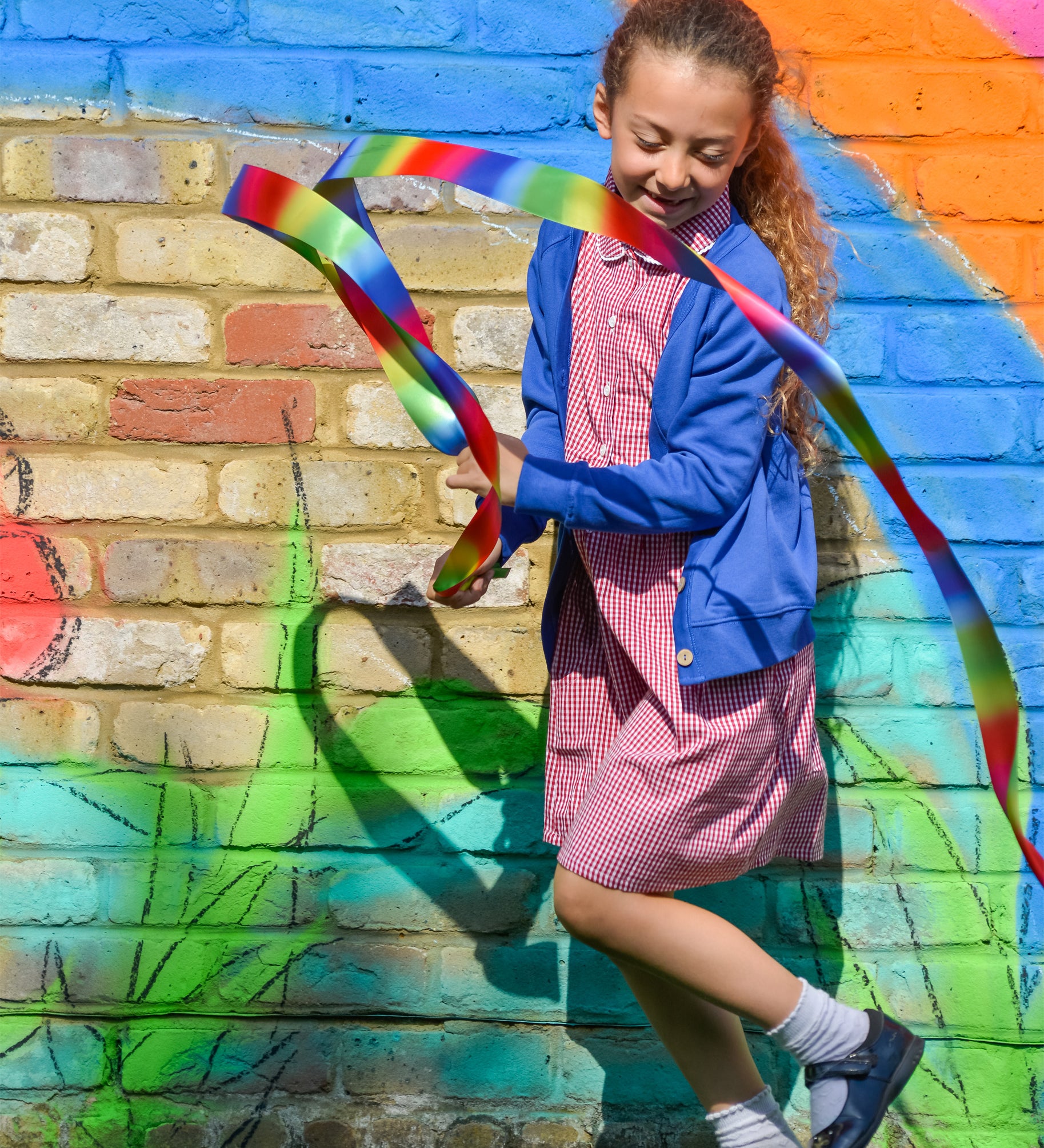 A little girl playing in the schoolyard, wearing the Eco Outfitters organic and fair trade cotton gingham summer dress and school cardigan in blue.