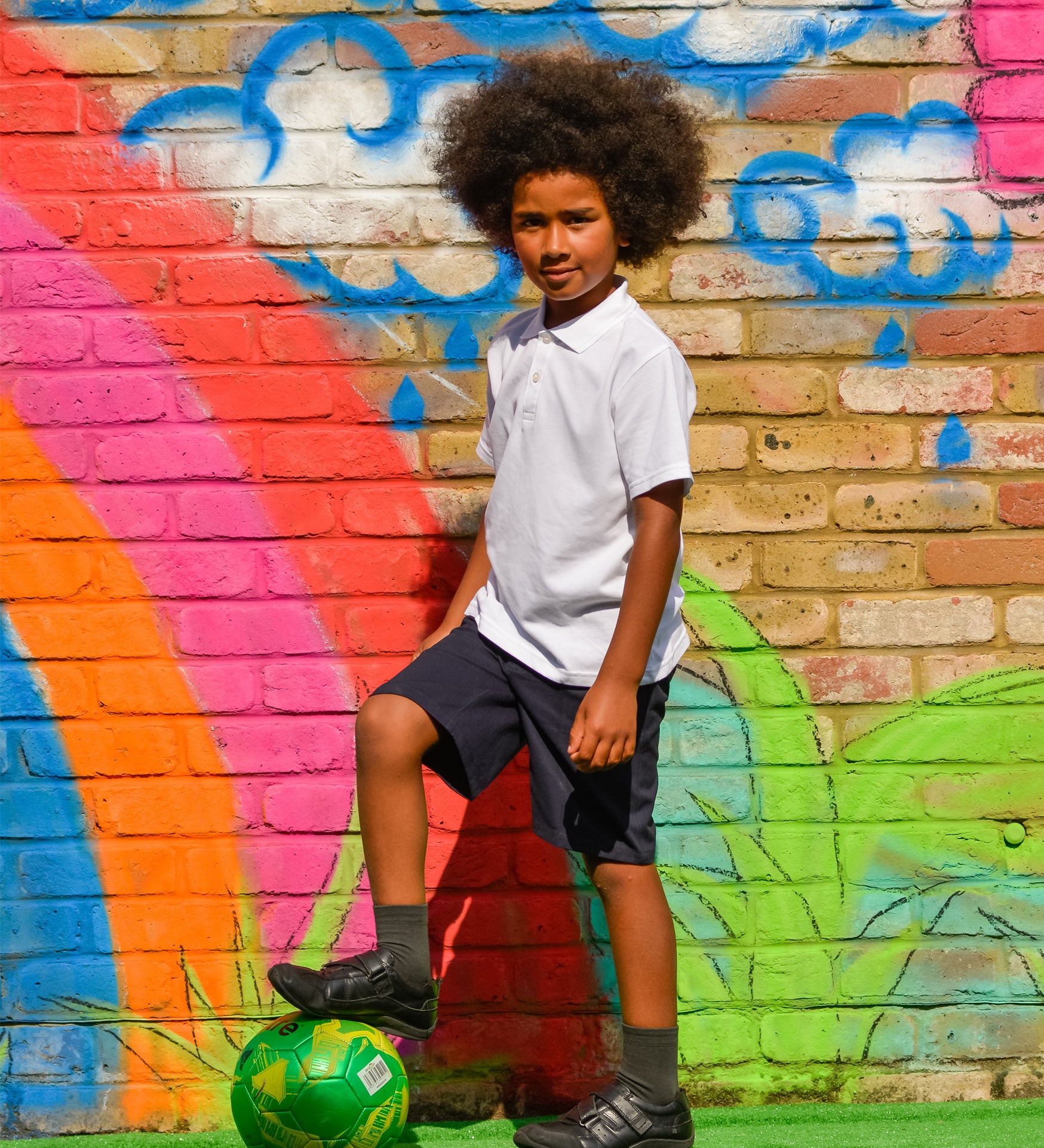 A child wearing the white Eco Outfitters organic school polo shirt and shorts, whilst playing football in the garden.