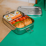 The Elephant Box Jumbo 2-in-1 stainless steel lunch box, the small pot is filled with sushi, and the larger box contains sausage rolls and tomatoes.