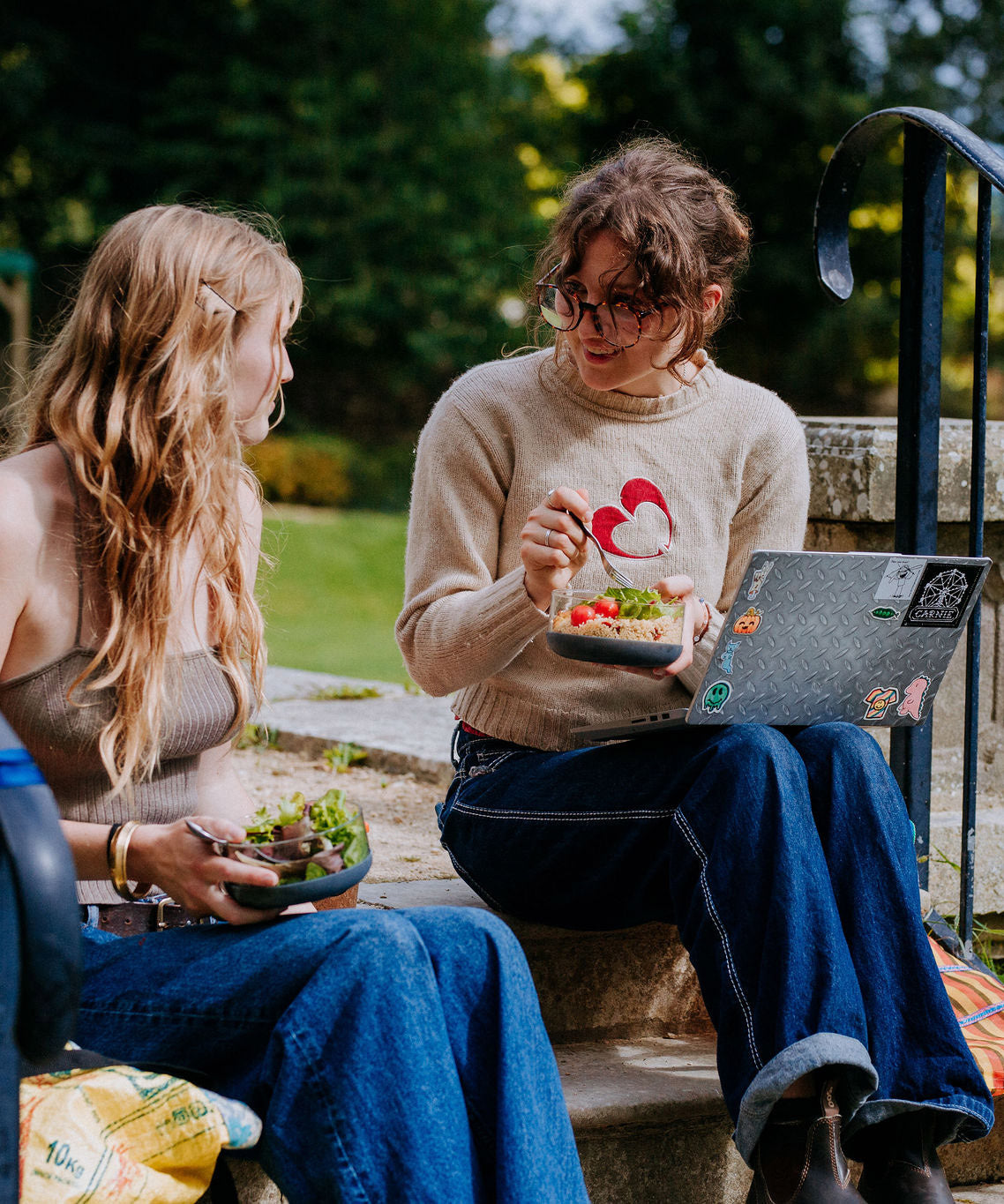 2 women sitting on stairs and eating food from the Elephant box bowls. The medium and large bowl are both available at Babipur.